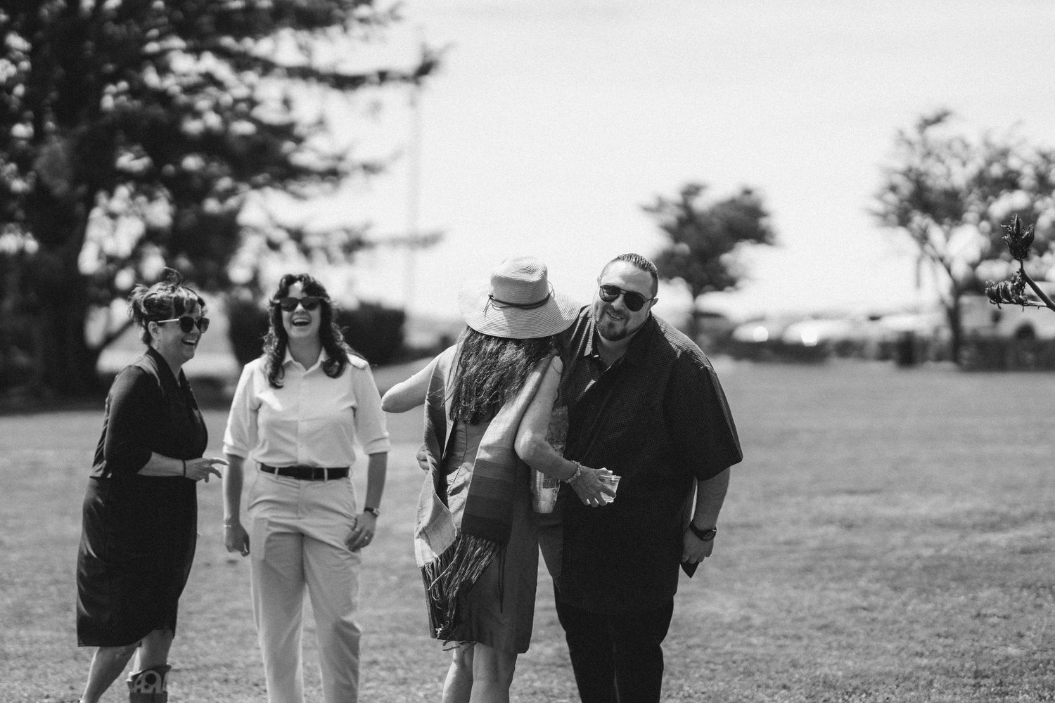 Black and white photo of four wedding guests laughing and walking together across a grassy field.