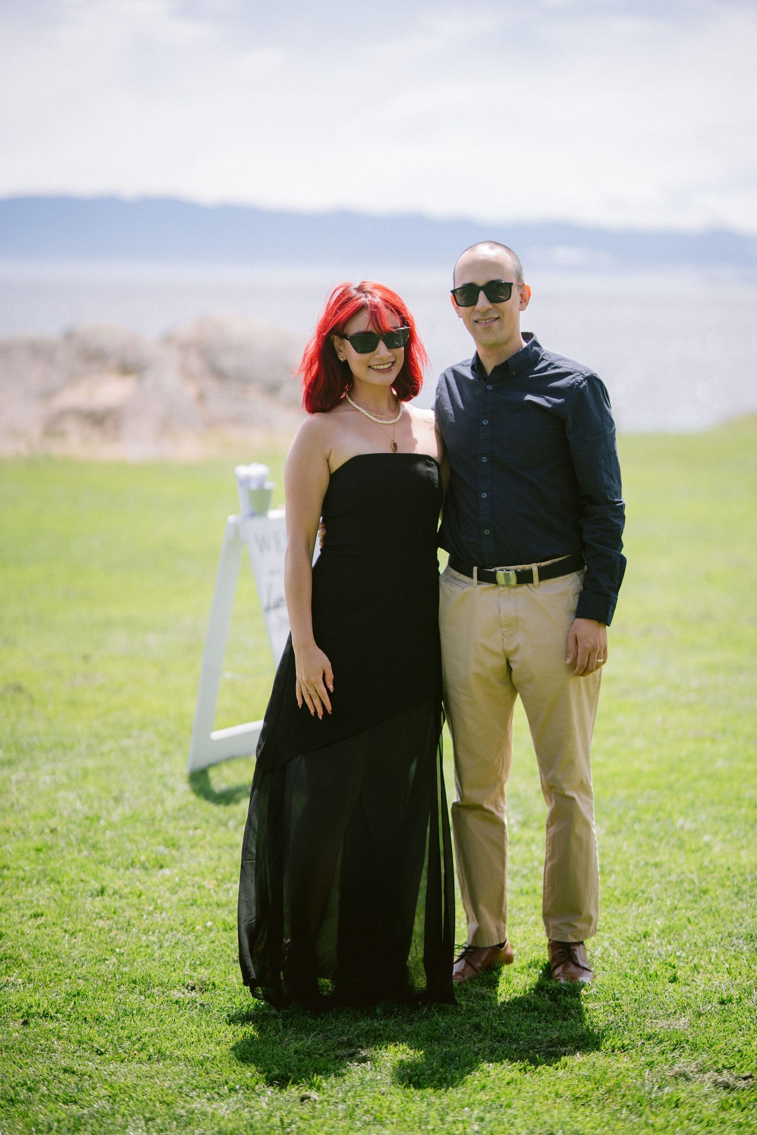 Couple posing outdoors at a wedding, woman in black gown with red hair and man in navy shirt and khakis.