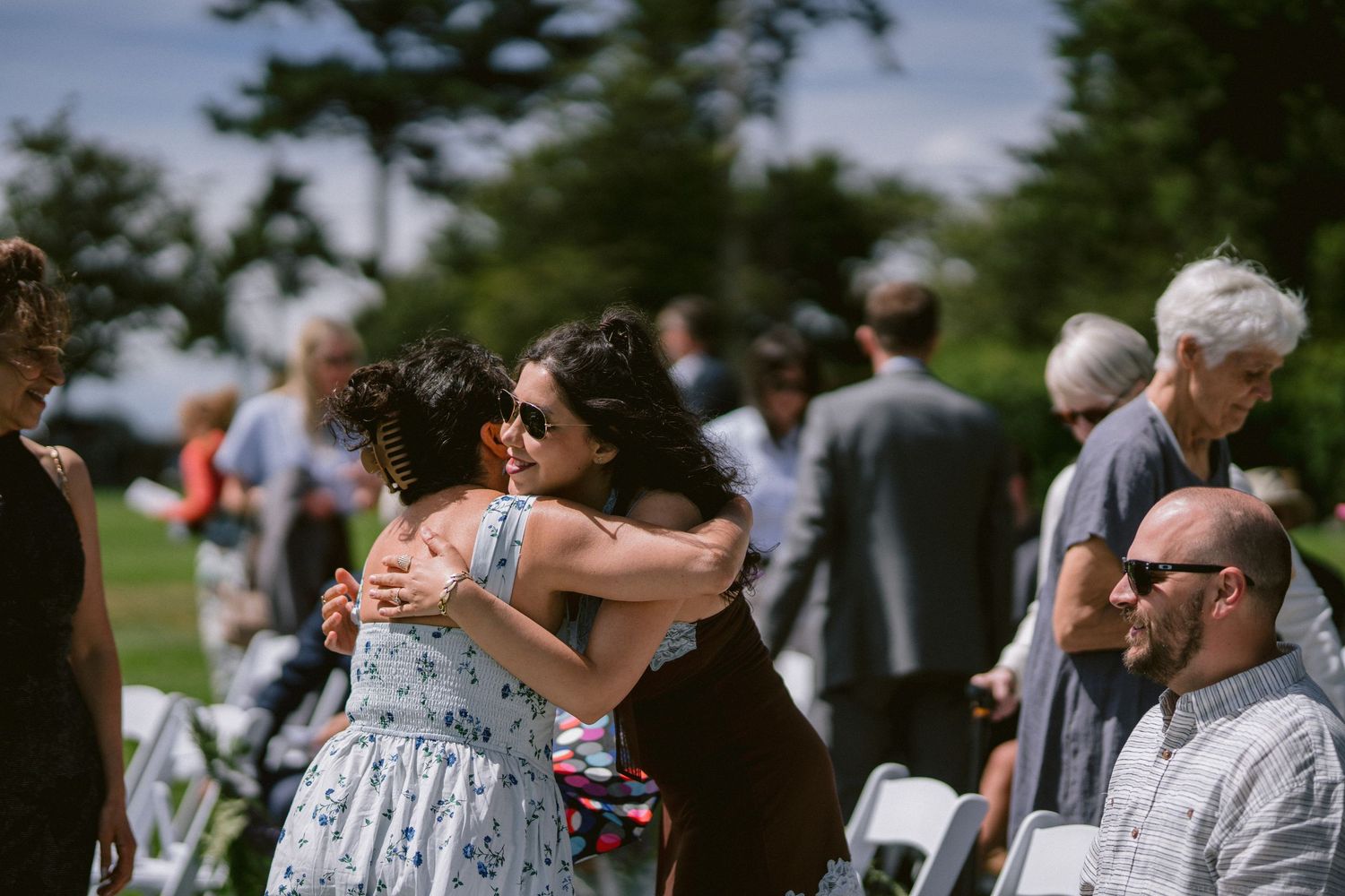 Guests embracing and mingling outdoors at a wedding ceremony on a sunny day.