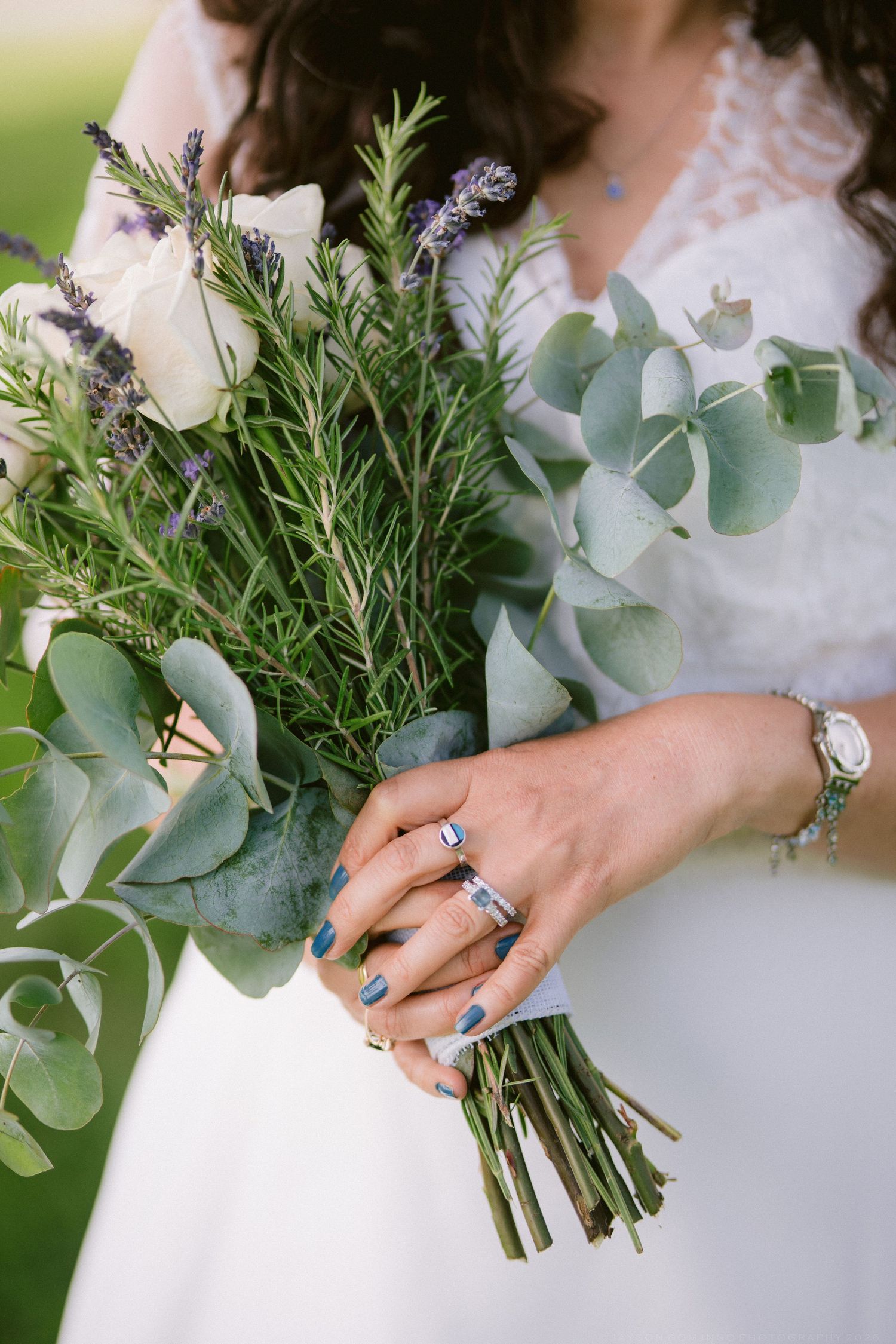 Bride holding rustic wedding bouquet with eucalyptus, lavender, and roses, wearing diamond ring.