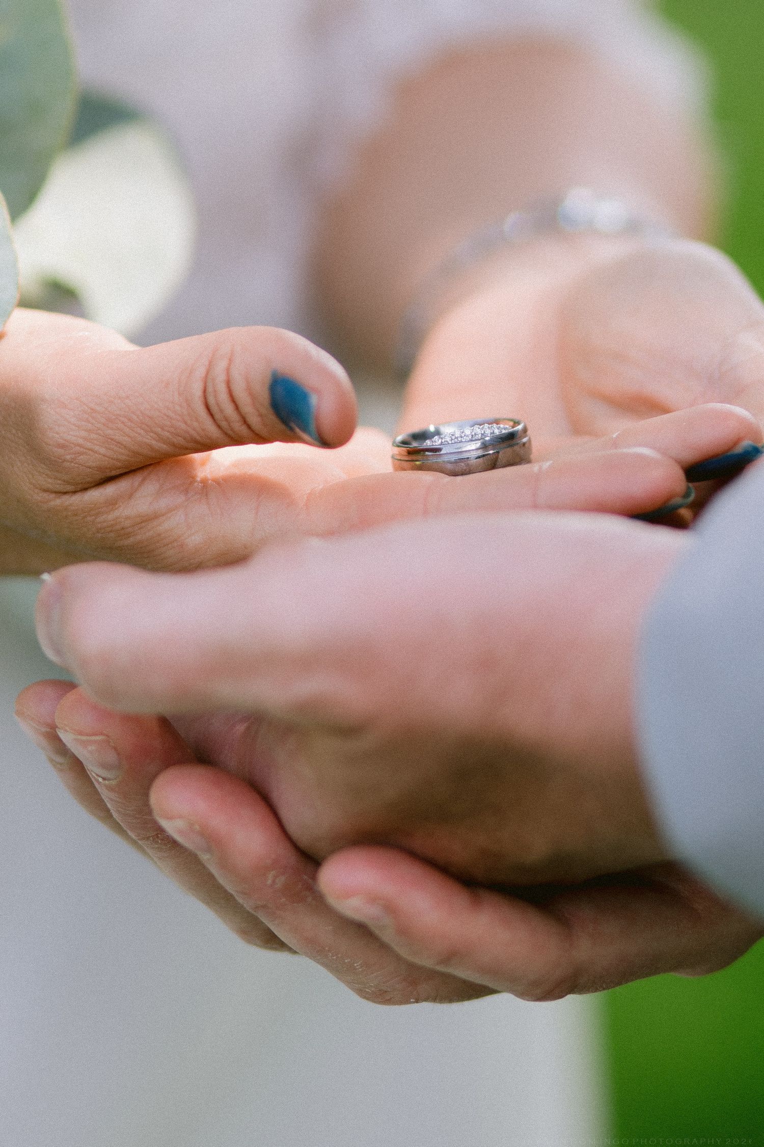 Close-up of couple's hands holding two wedding rings during an outdoor ring exchange ceremony.