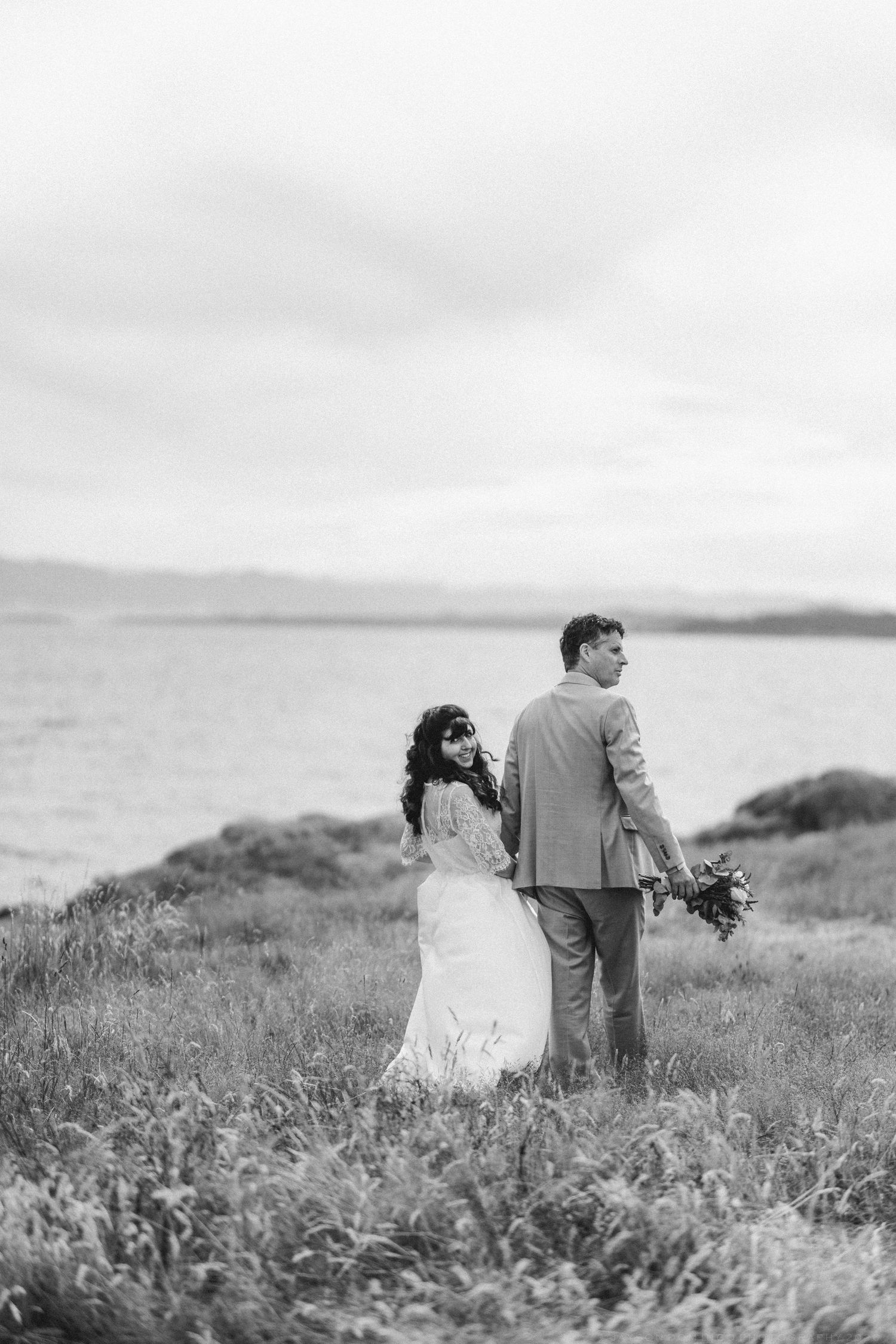 Black and white photo of bride and groom standing back to back by the sea.