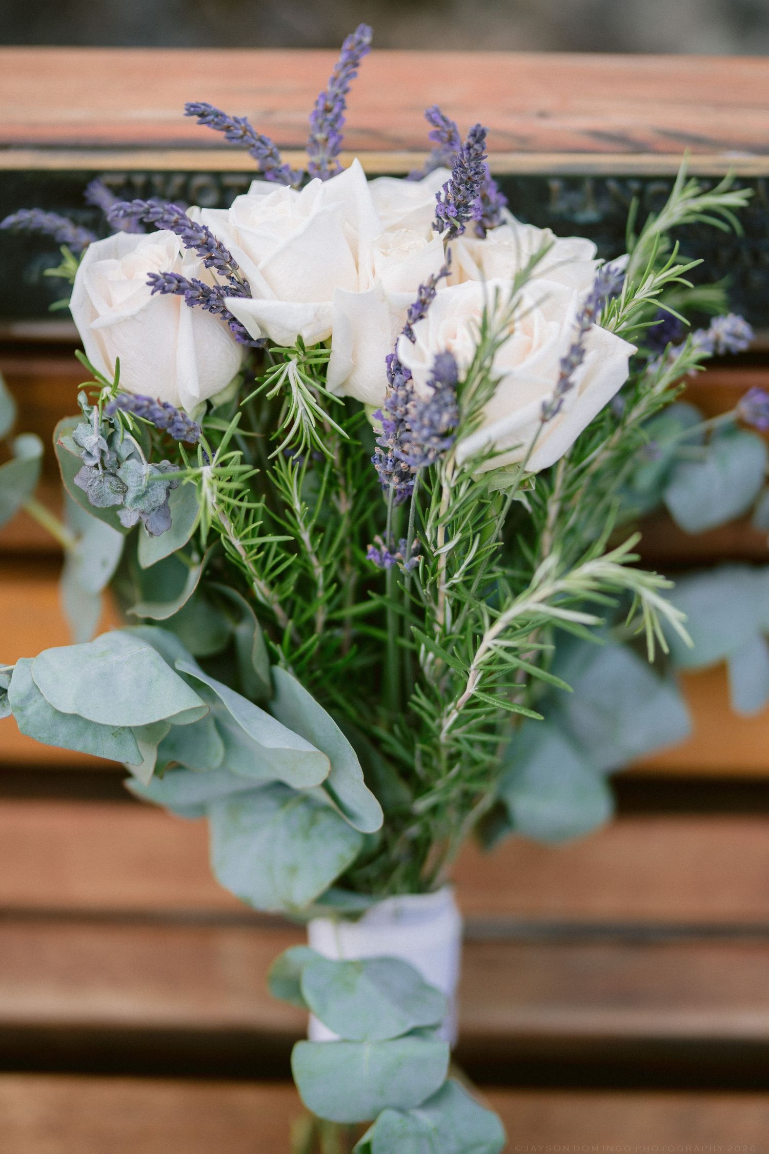 Elegant wedding bouquet featuring white roses, lavender, rosemary, and eucalyptus tied with white ribbon.