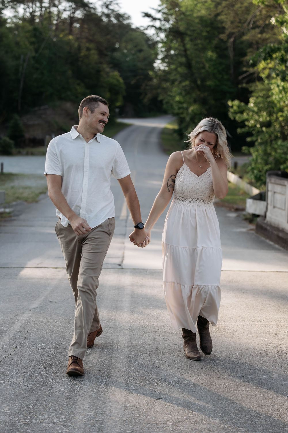Happy couple holding hands walking down a scenic road, man in white shirt and woman in flowing white dress.