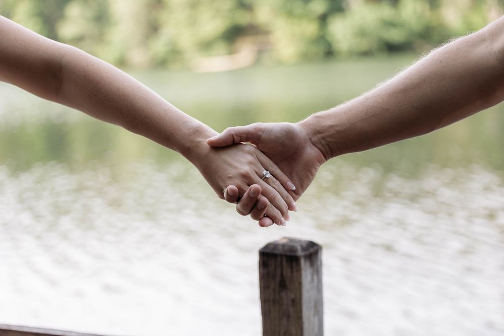 Two people holding hands near a serene lake, symbolizing connection, love, and togetherness outdoors.