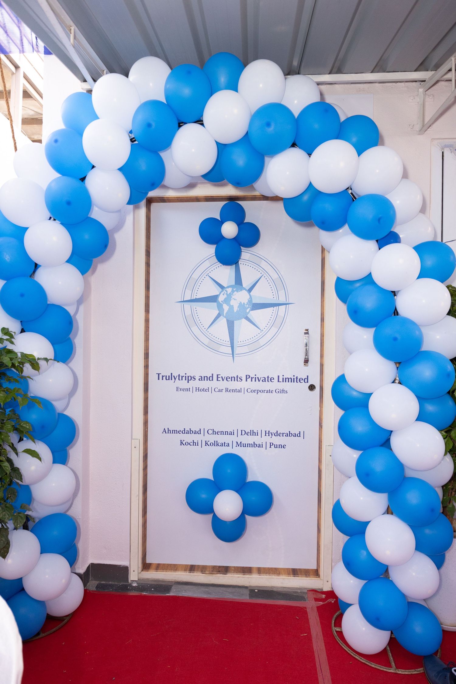 Blue and white balloon arch decorating the entrance of Trulytrips and Events Private Limited office.