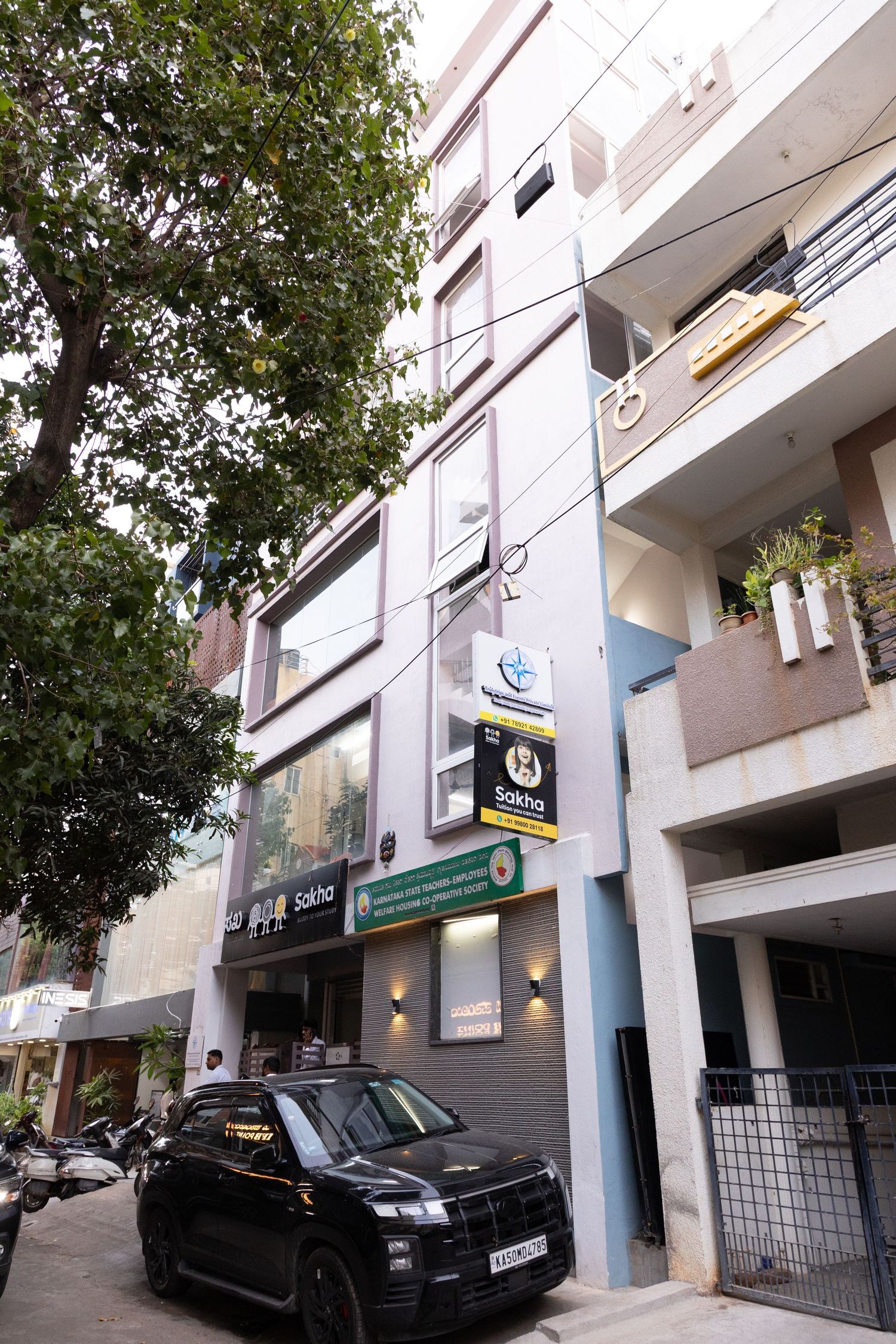 Multi-story commercial building with shops and offices, black SUV parked outside, urban street setting in India.
