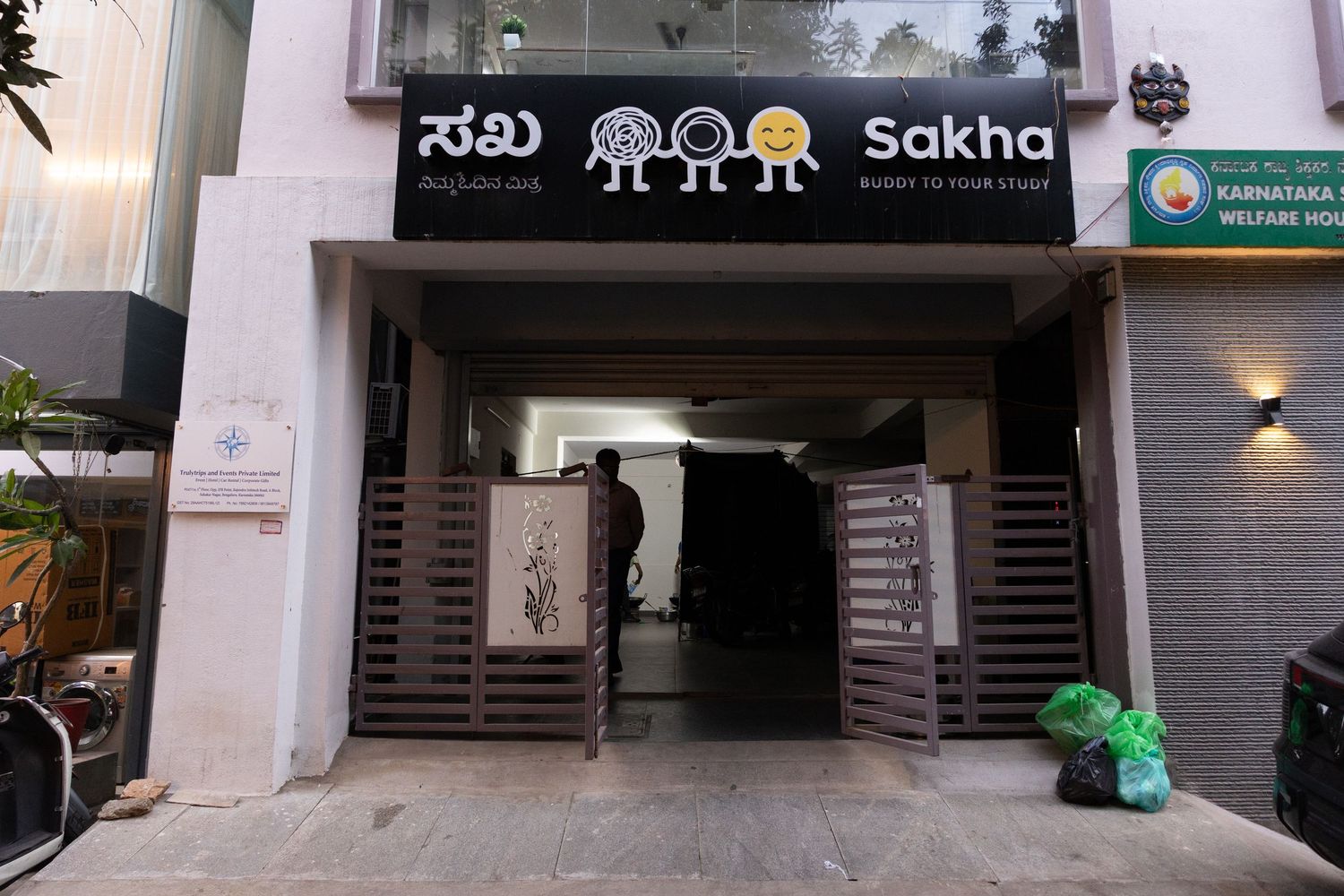 Sakha restaurant entrance with Kannada signage, wooden gates, and Karnataka Welfare sign on a city street.