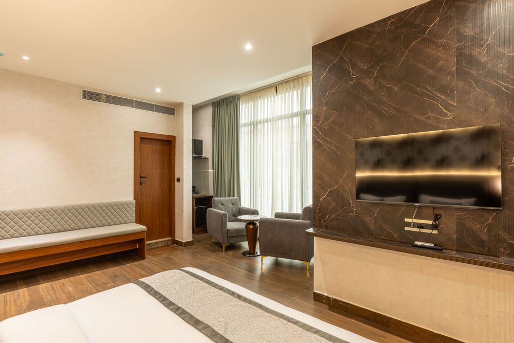Modern hotel room featuring a marble TV wall, plush seating area, large window, and hardwood floors.
