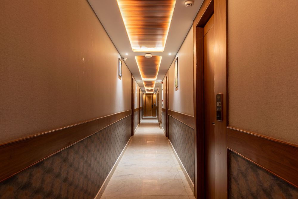Elegant hotel corridor with warm lighting, decorative ceiling, patterned walls, and carpeted floor extending into the distance.