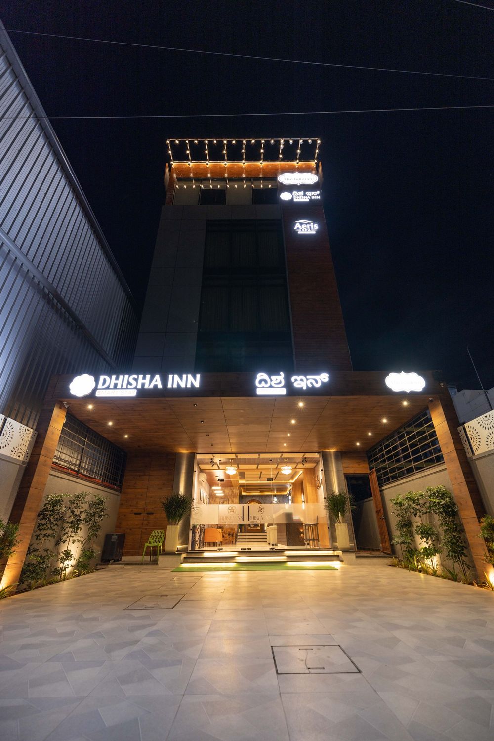 Dhisha Inn hotel exterior illuminated at night with warm lights, modern multi-story facade, and welcoming entrance in India.