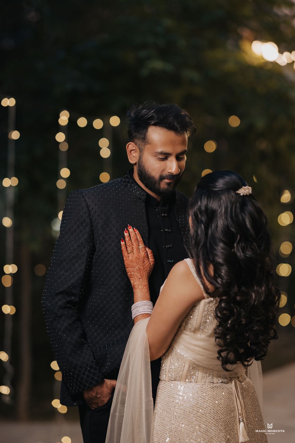 Couple in elegant wedding attire sharing a romantic moment with bokeh fairy lights in the background.
