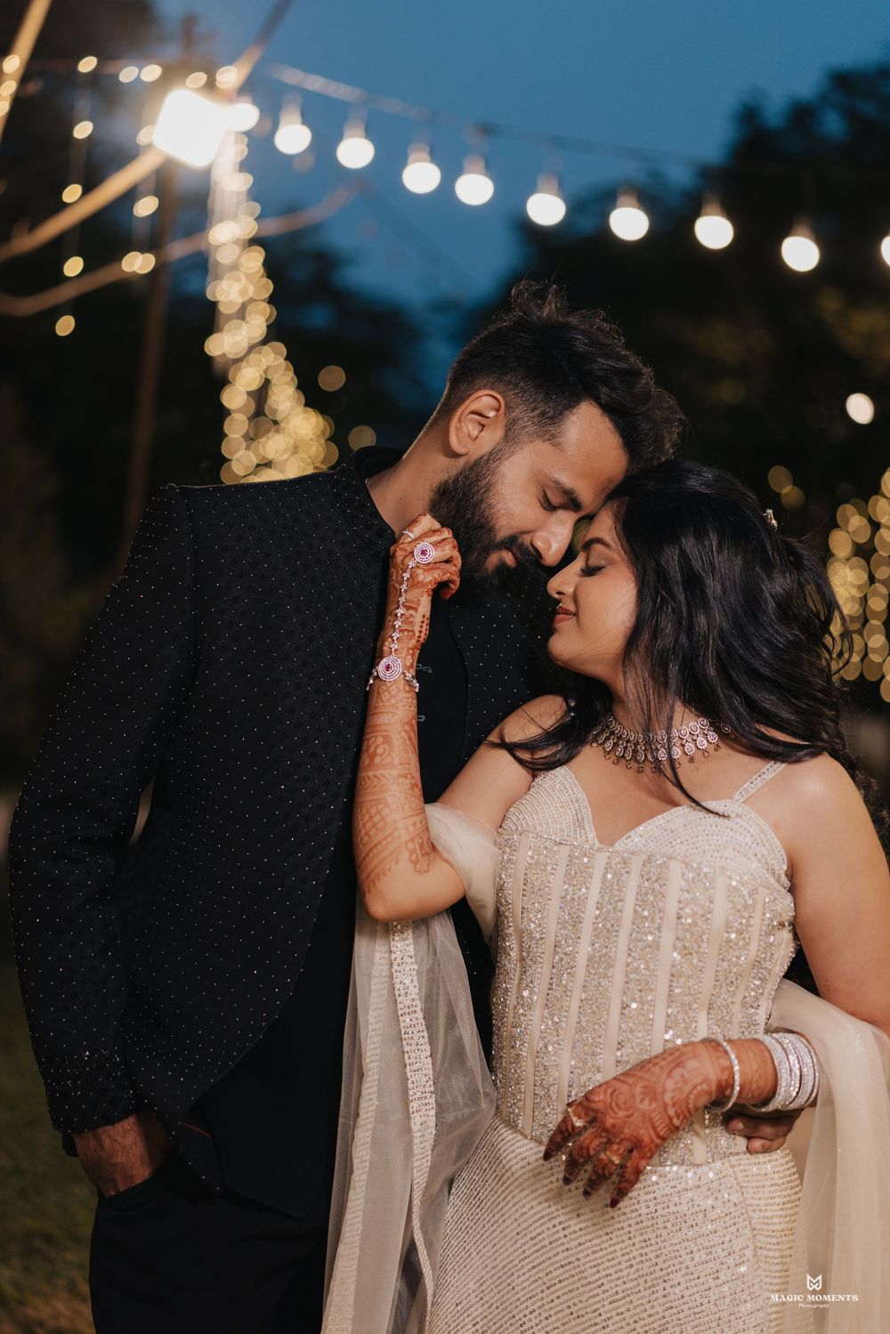 Romantic couple in wedding attire share an intimate moment under string lights at an outdoor evening celebration.