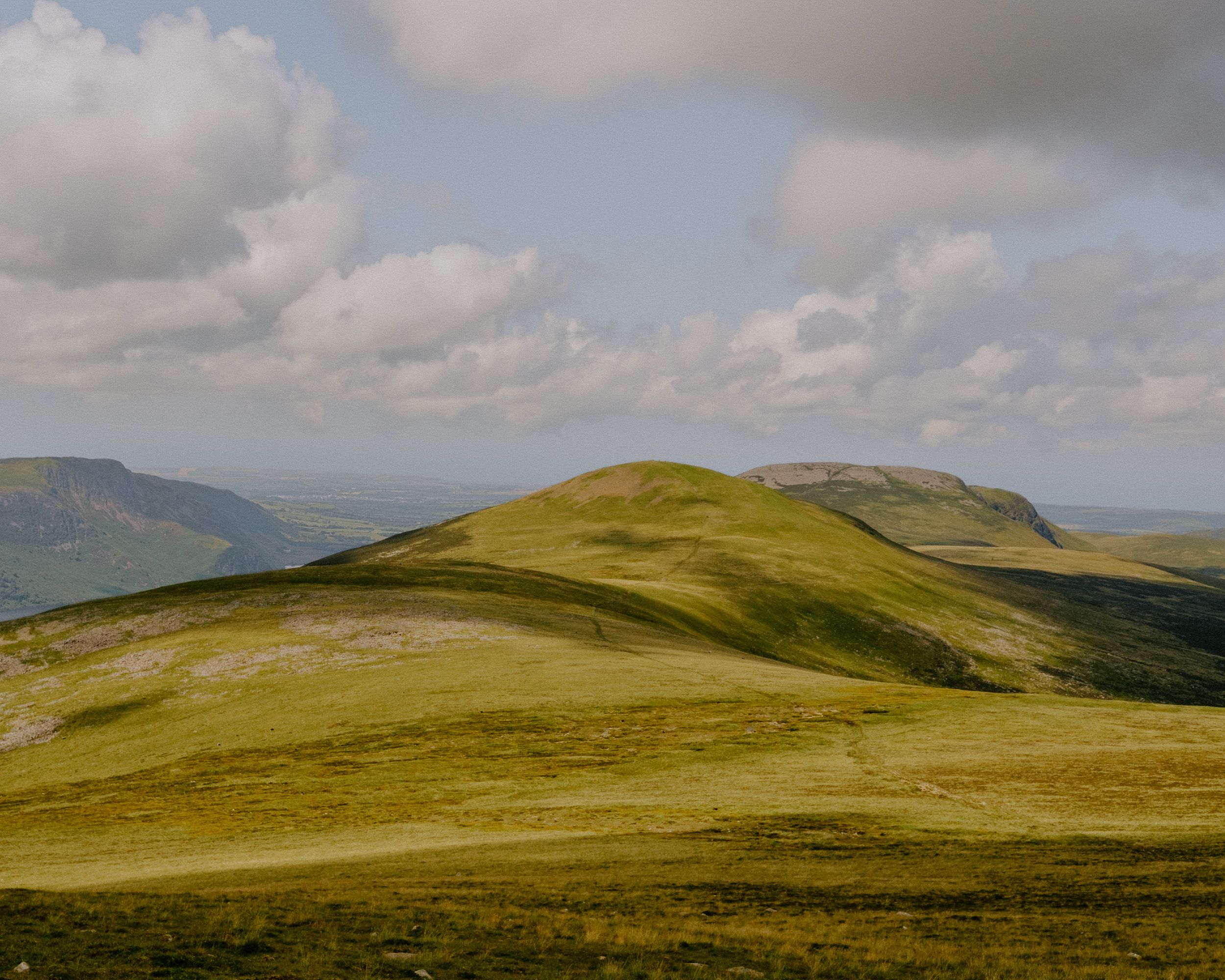Rolling green hills under a partly cloudy sky in a scenic Welsh mountain landscape with sweeping valley views.