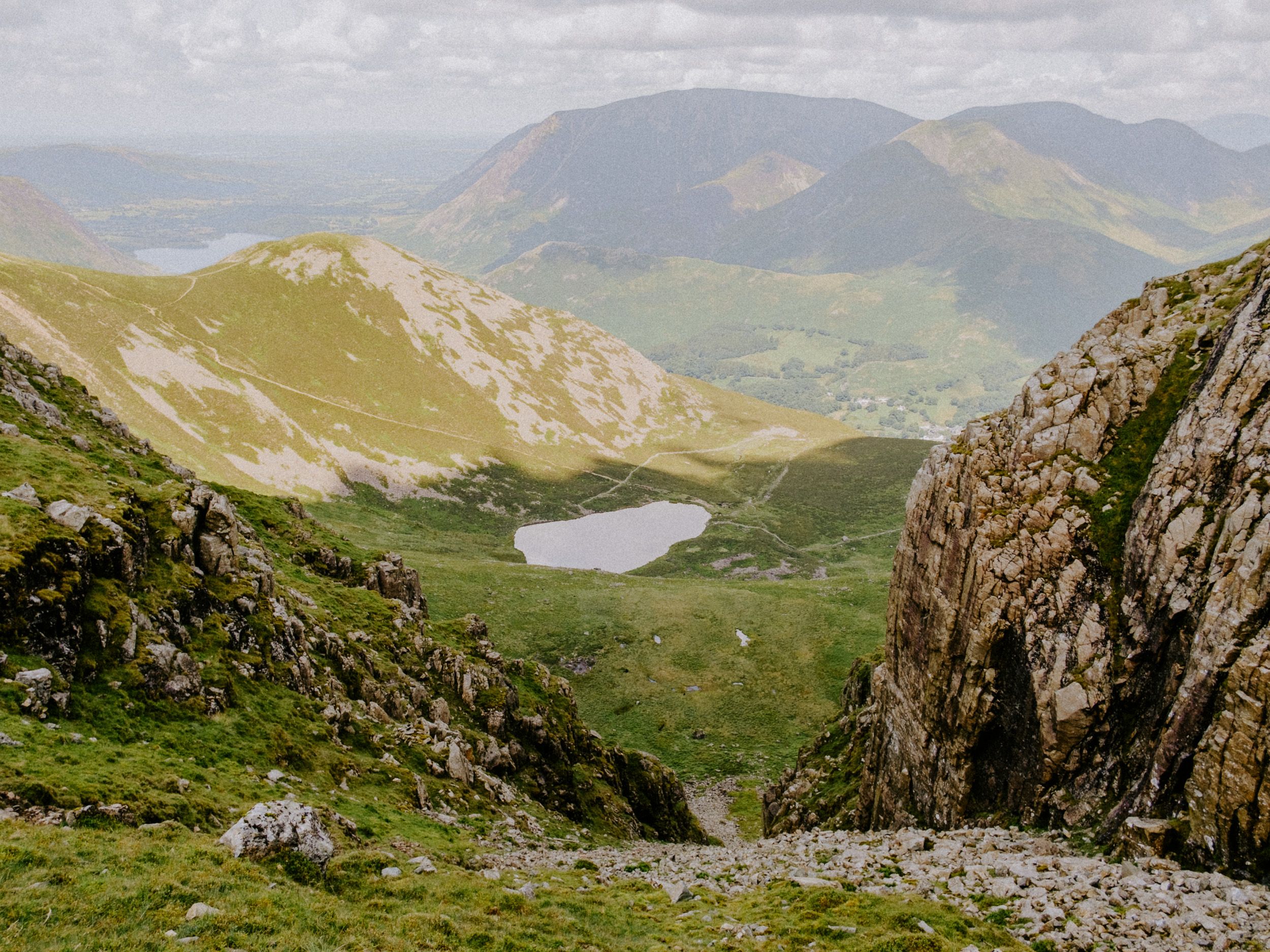 Scenic mountain valley view with a glacial lake, green slopes, and distant peaks under a cloudy sky in Snowdonia, Wales.