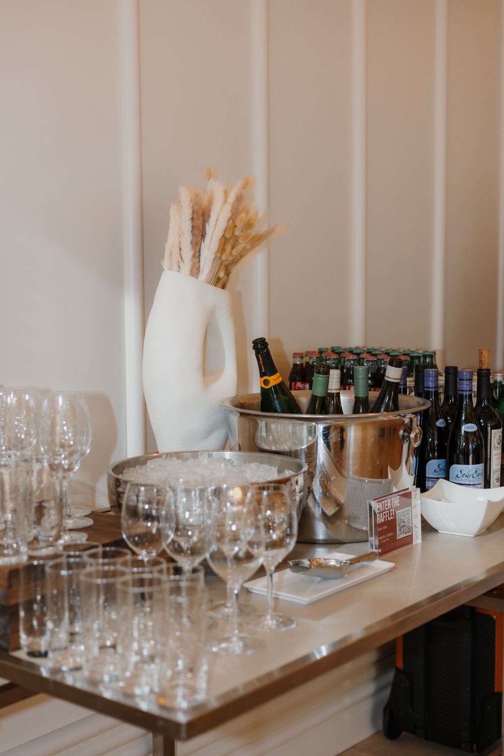 Elegant bar setup with wine glasses, champagne on ice, and assorted bottles on a wooden table at an event.