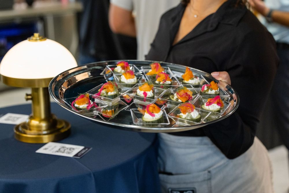 Server holding a silver tray of elegant bite-sized appetizers with colorful toppings at a catered event.