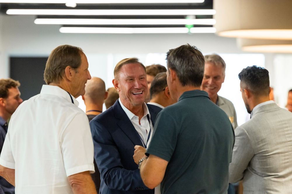 Group of men in business casual attire laughing and networking at an indoor corporate event.