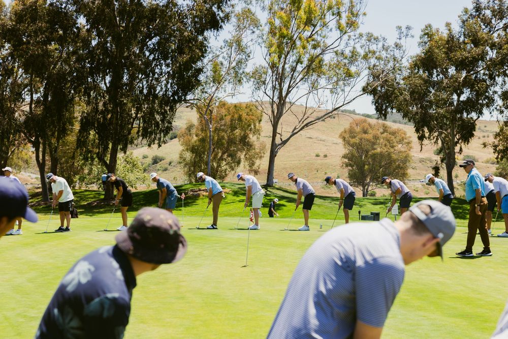 Group of golfers practicing putting on a sunny green golf course surrounded by eucalyptus trees.
