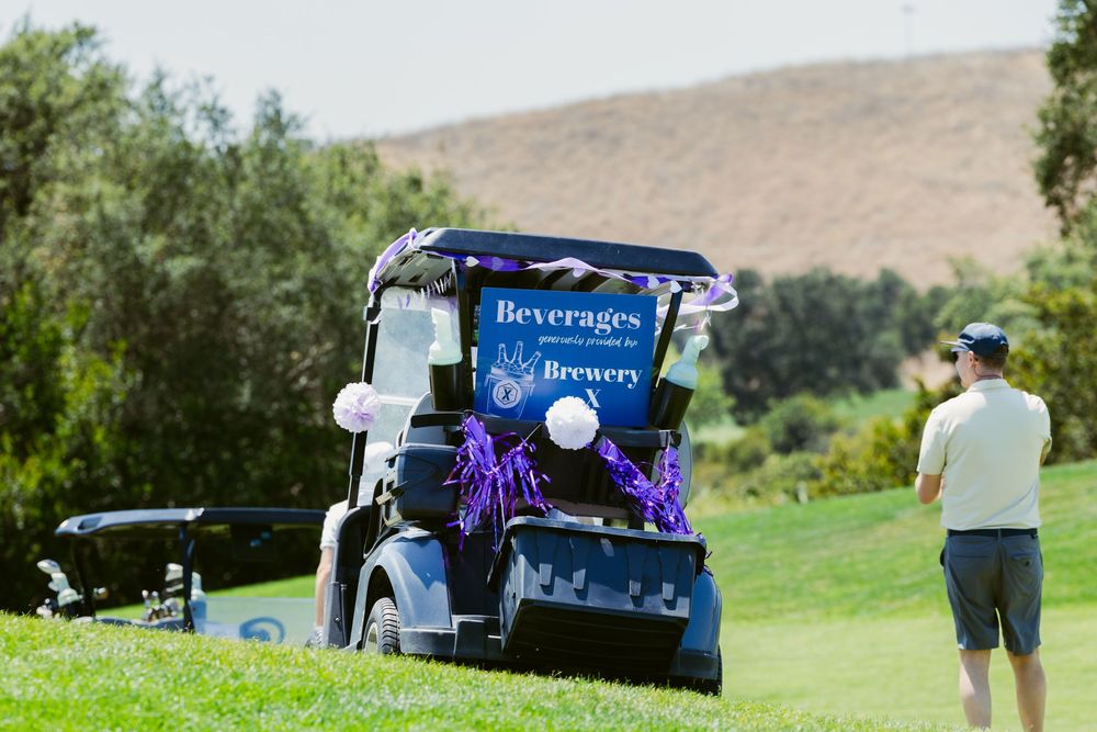 Golf cart beverage station from a brewery on a sunny green golf course, with a man standing nearby.