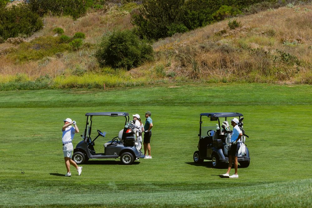 Golfers playing on a scenic green golf course with two golf carts on a sunny day.