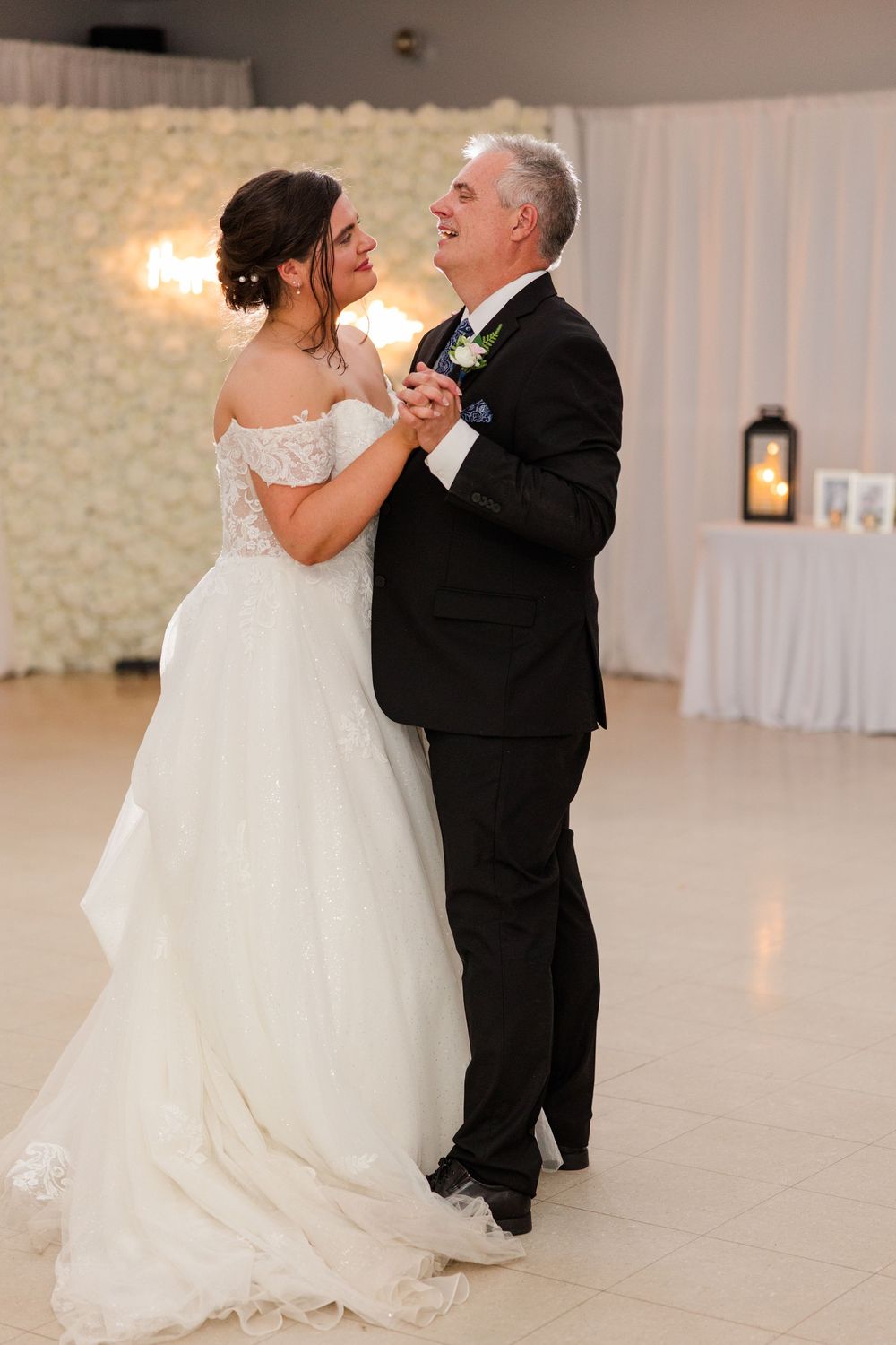 Bride and father share an emotional first dance at wedding reception with floral backdrop.