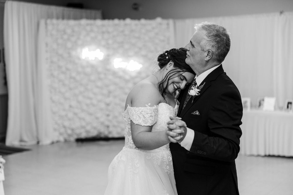 Black and white photo of a bride and her father sharing an emotional first dance at a wedding reception.