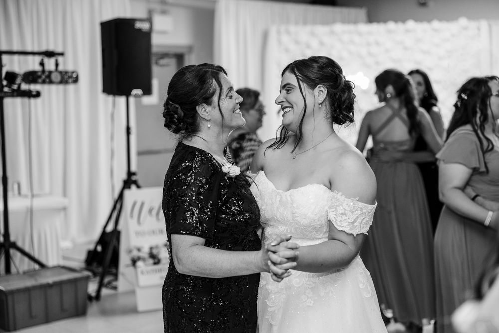 Bride and older woman share emotional dance at wedding reception in black and white photo.