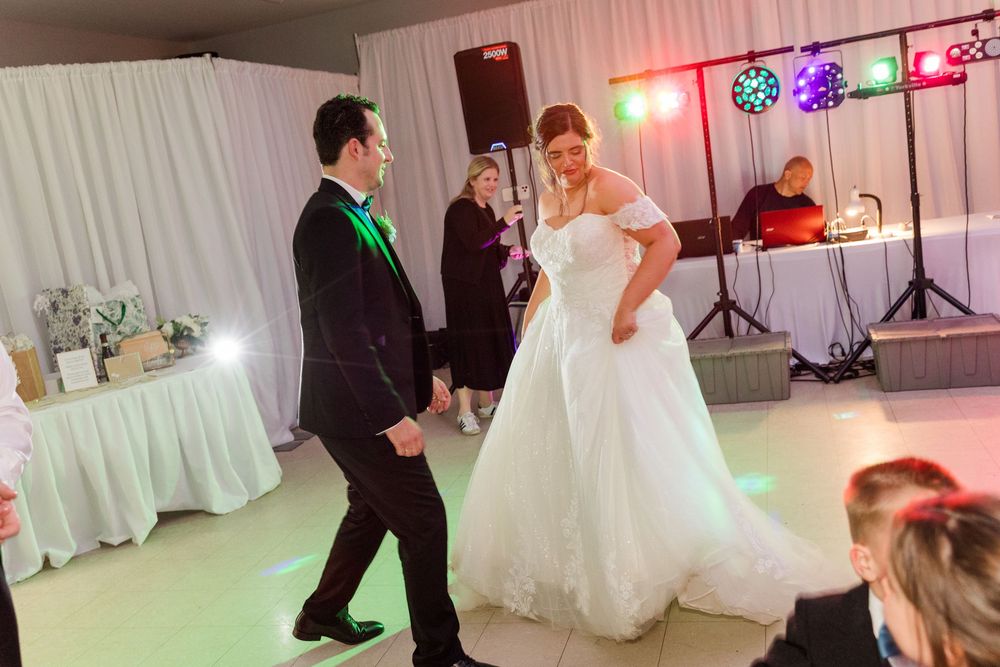 Bride and groom share their first dance at a wedding reception with a DJ and colorful lights in the background.
