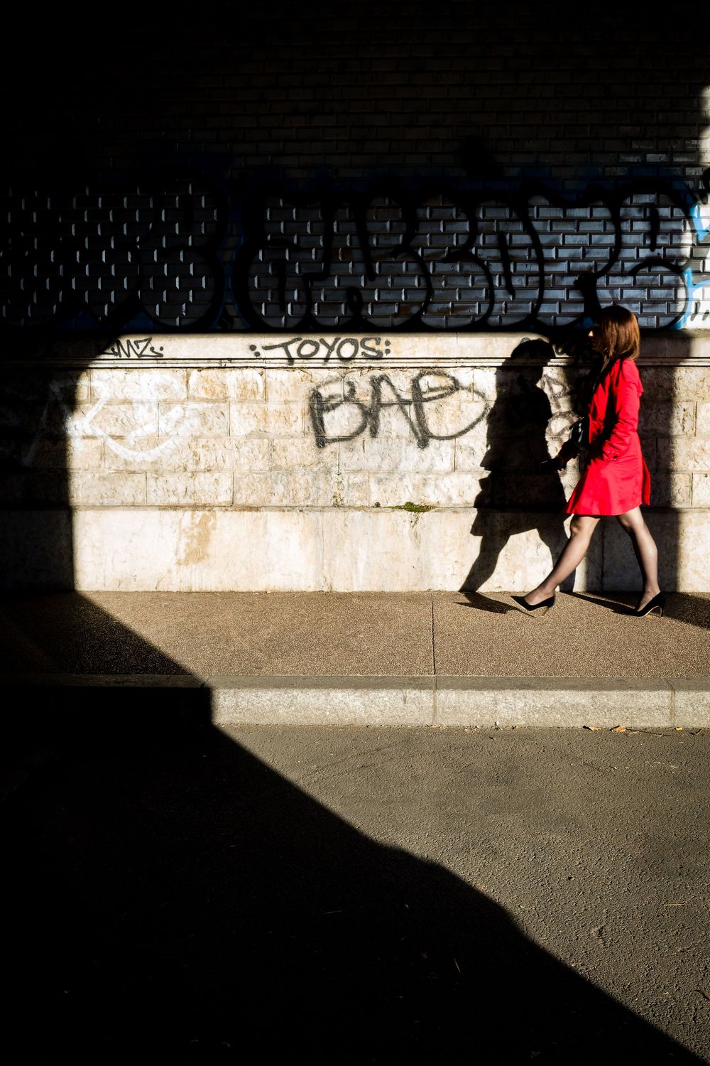 Passante en robe rouge traversant une zone de lumière et d'ombre dans une rue de Lyon.
