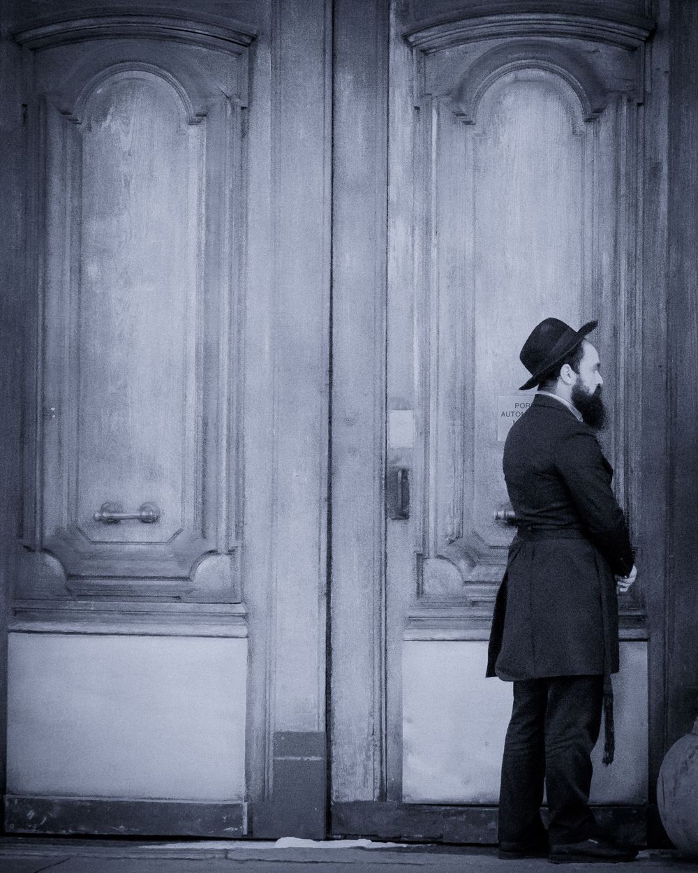 Homme debout devant une grande porte ancienne, photographié en noir et blanc.