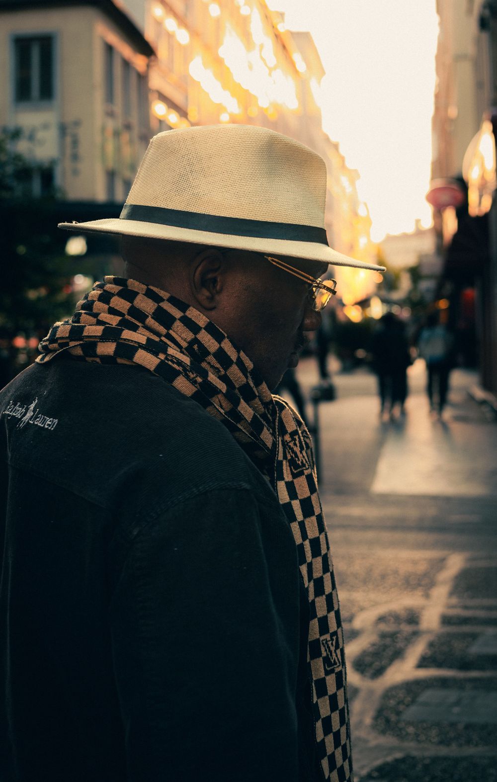 Passant portant un chapeau et une écharpe dans une rue de Lyon éclairée par le soleil.