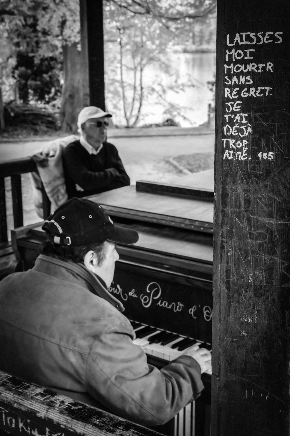 Deux hommes autour d’un piano public dans la rue, photographiés en noir et blanc.