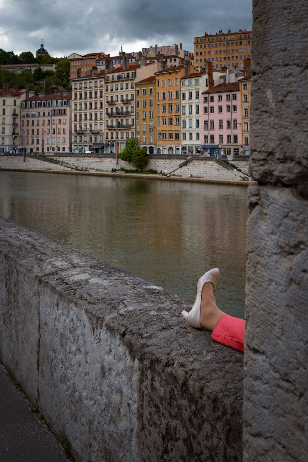 Vue sur les façades colorées du Vieux Lyon depuis les quais de Saône, avec une personne partiellement visible au premier plan.