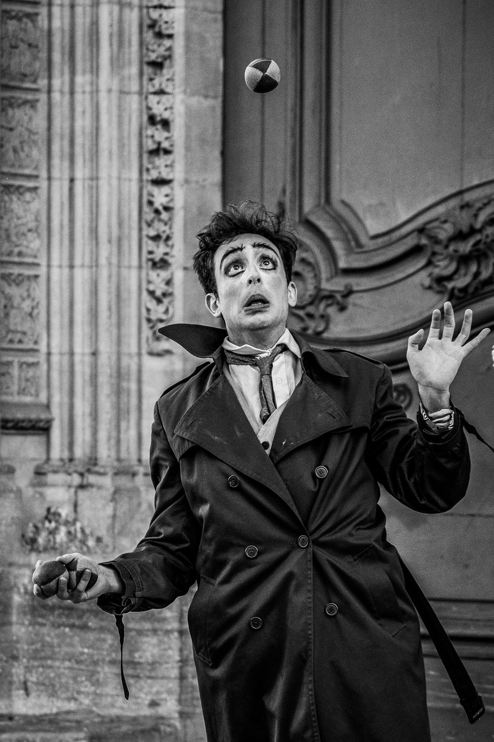 Artiste de rue en noir et blanc réalisant un numéro de jonglage devant une architecture ancienne.