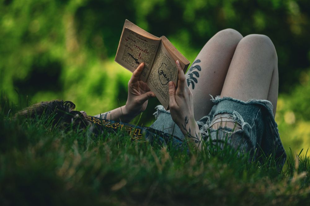 Personne allongée dans l'herbe lisant un livre, entourée de végétation.