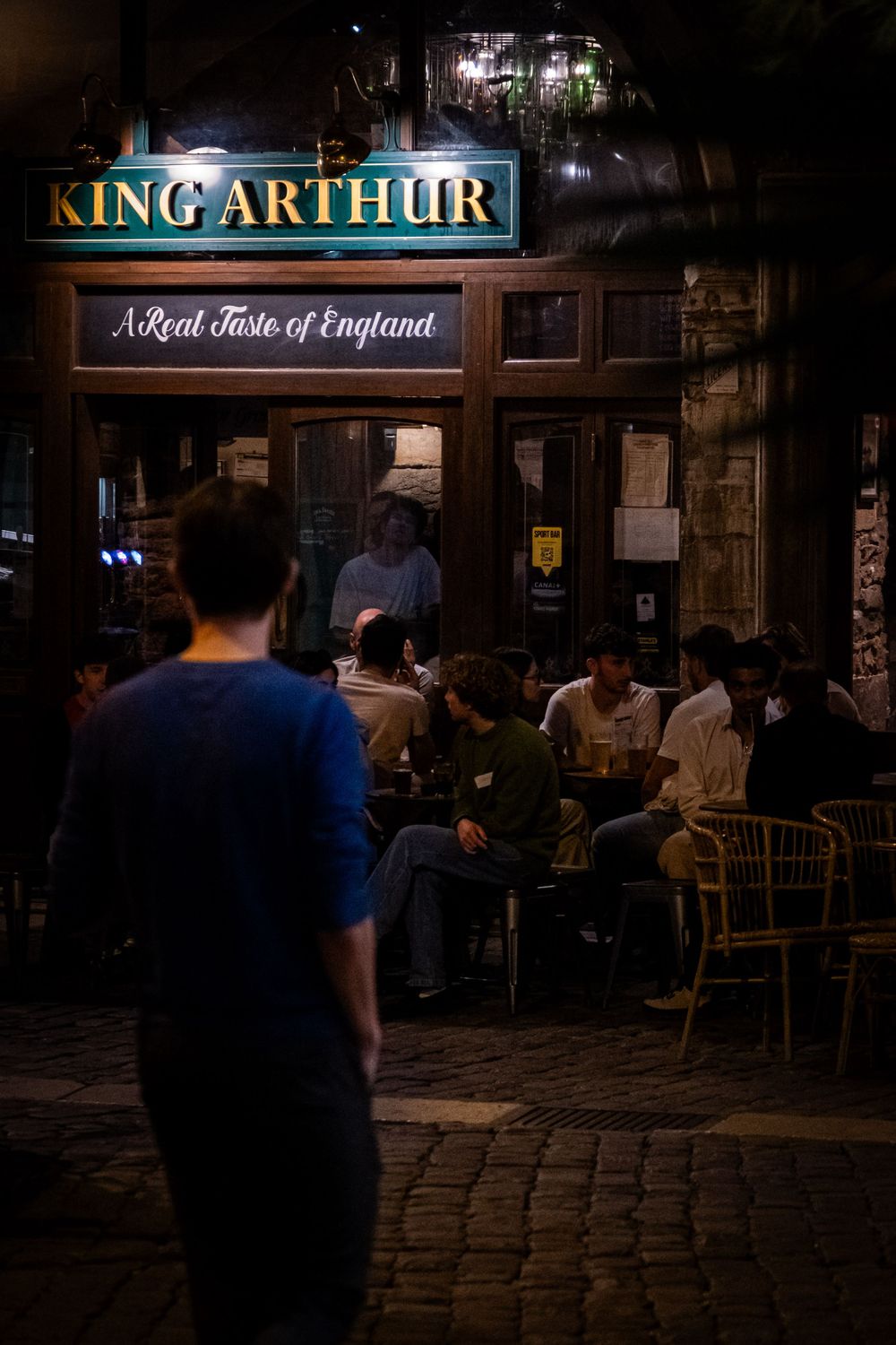 Silhouette d'un passant devant un pub animé dans une rue de Lyon la nuit.