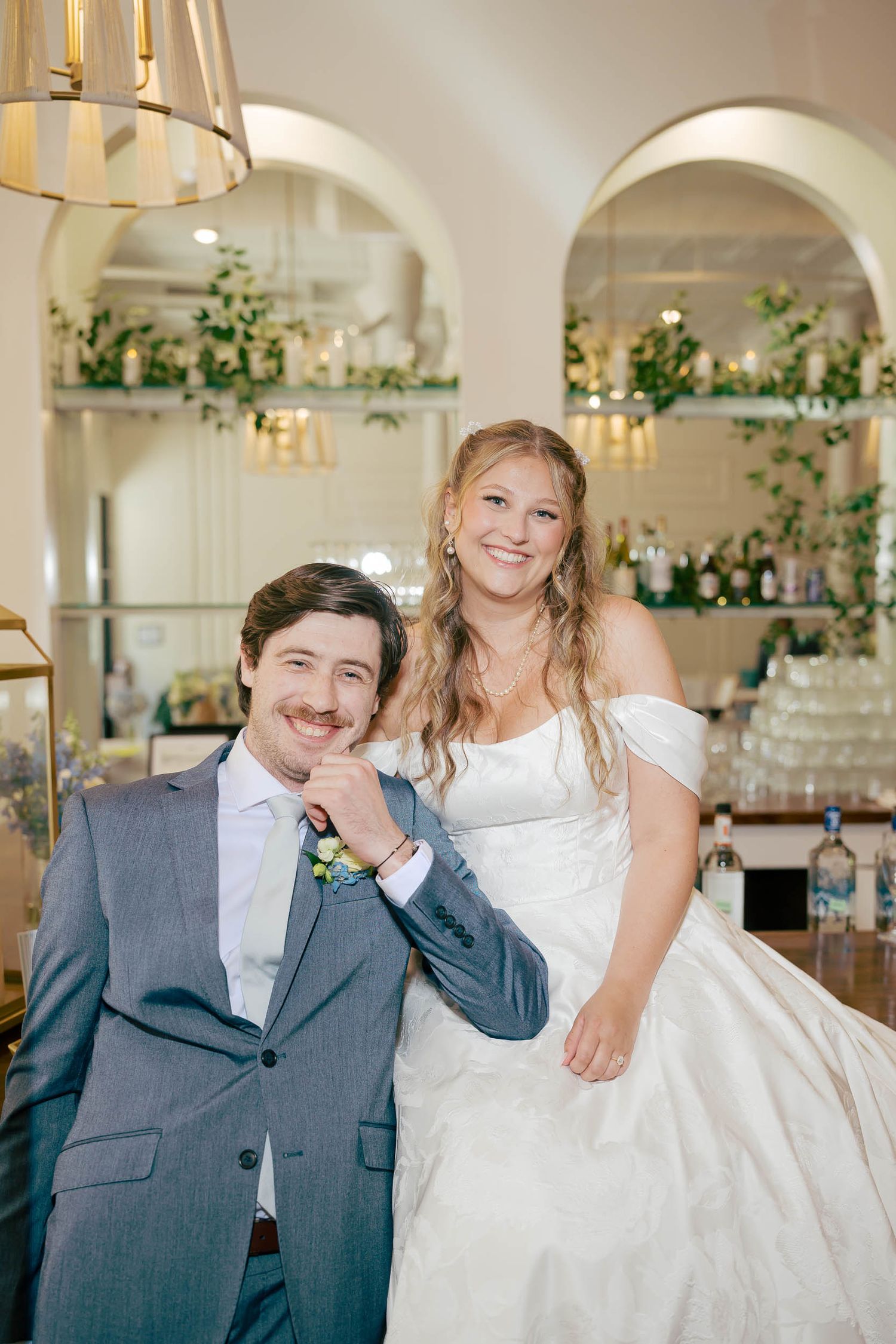 Elegant wedding ceremony venue with white draping, chandeliers, black chiavari chairs, and floral arrangements on white pillars.