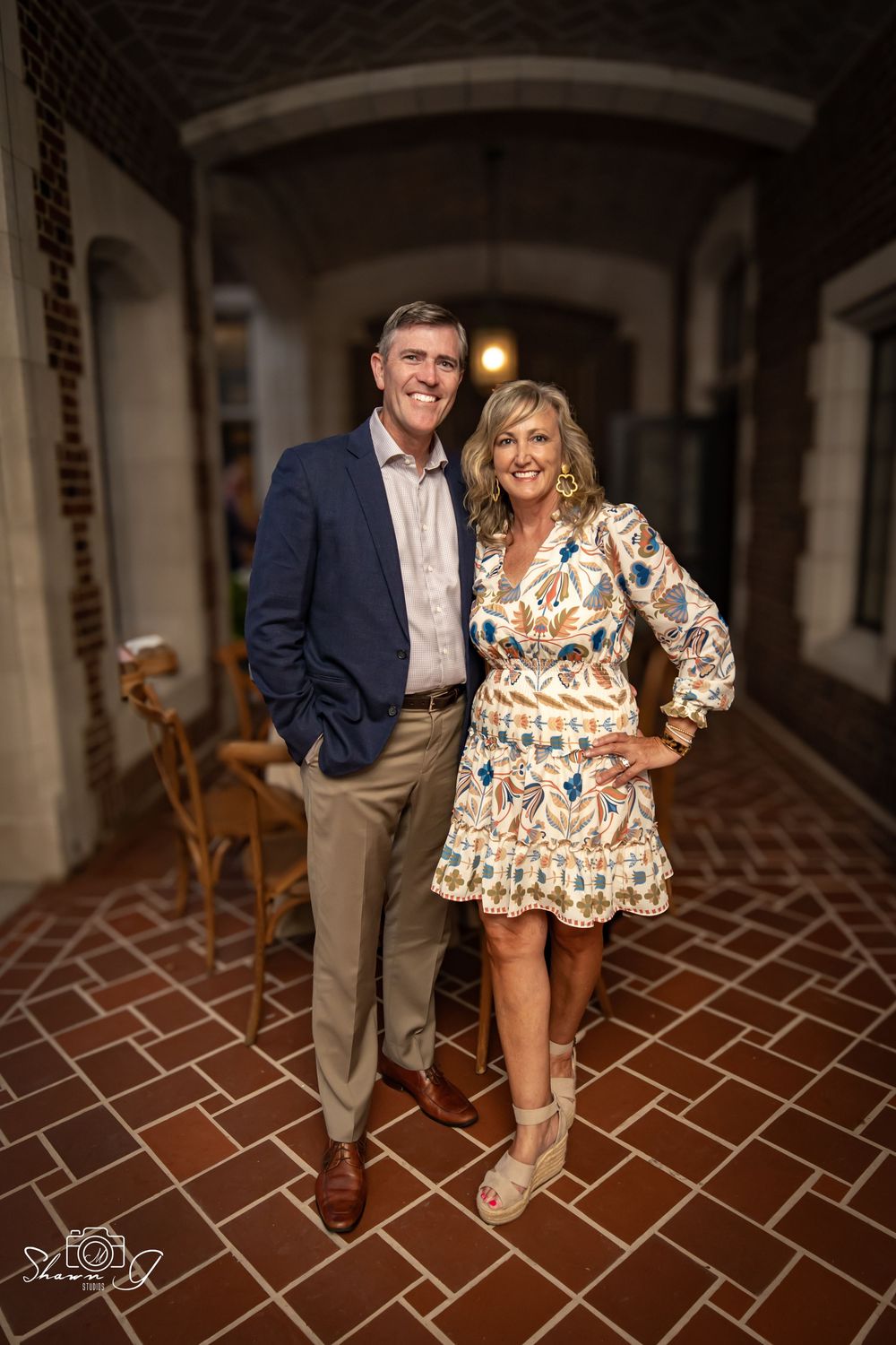 Couple posing in brick archway, man in navy blazer and woman in floral dress.