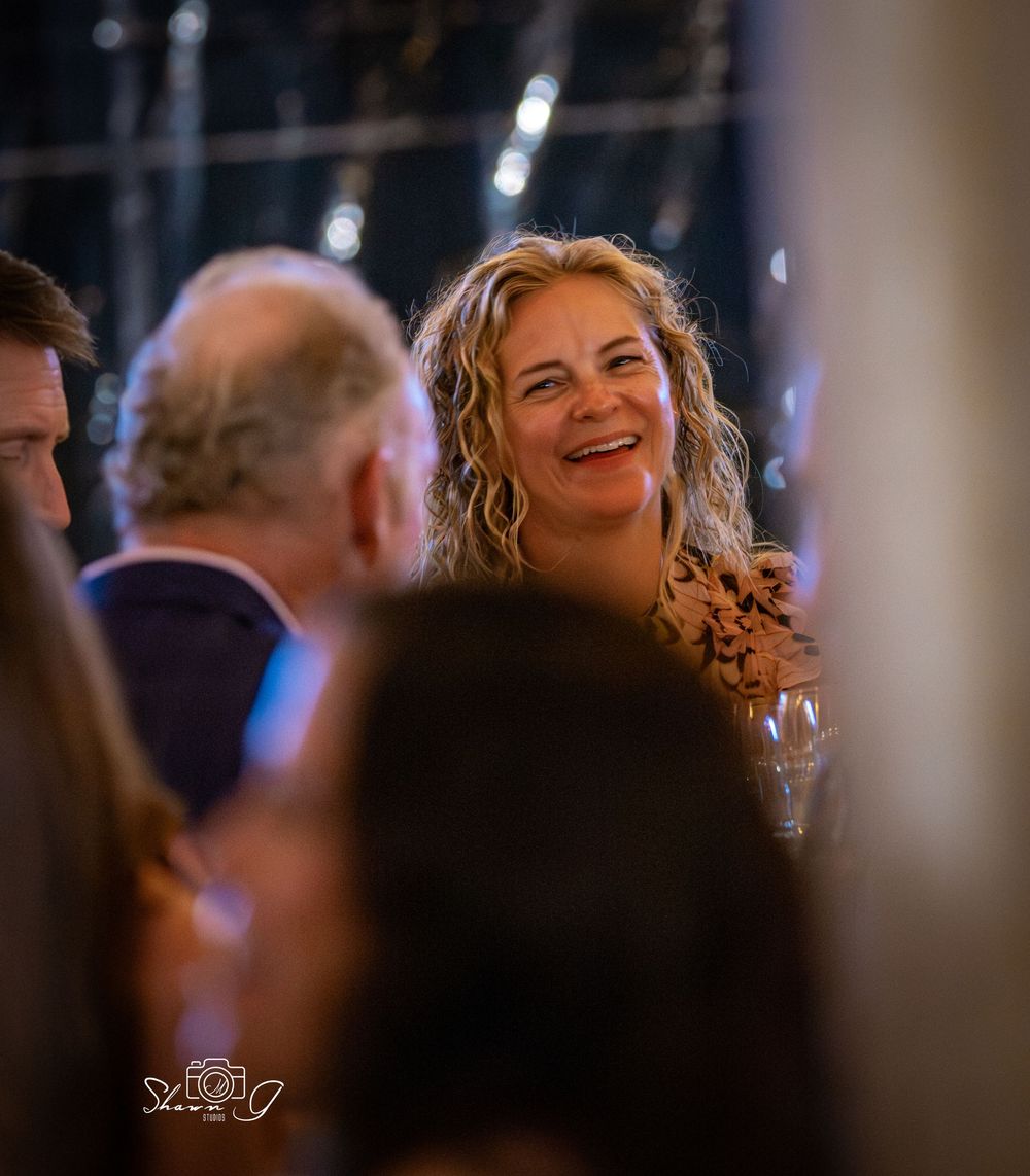A smiling woman with curly blonde hair laughing joyfully at an elegant evening social event.