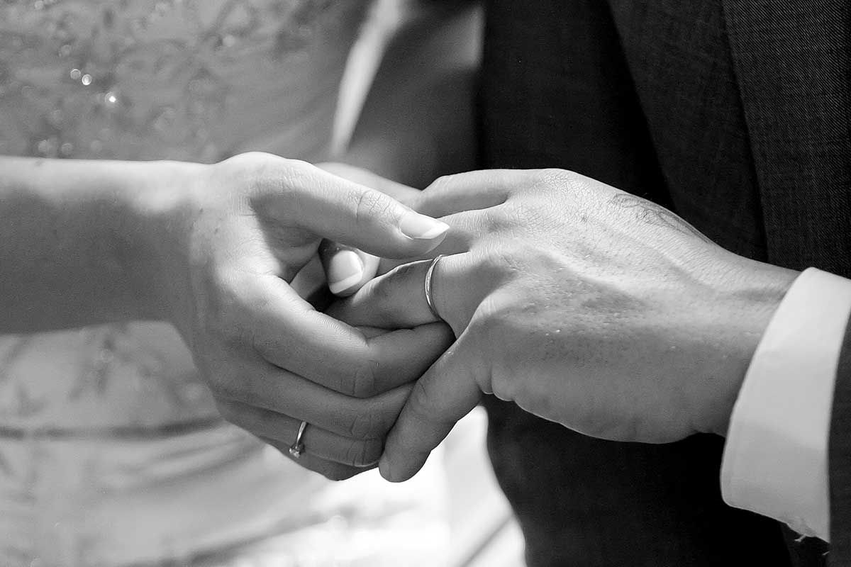 Black and white photo of a couple exchanging wedding rings during a marriage ceremony.