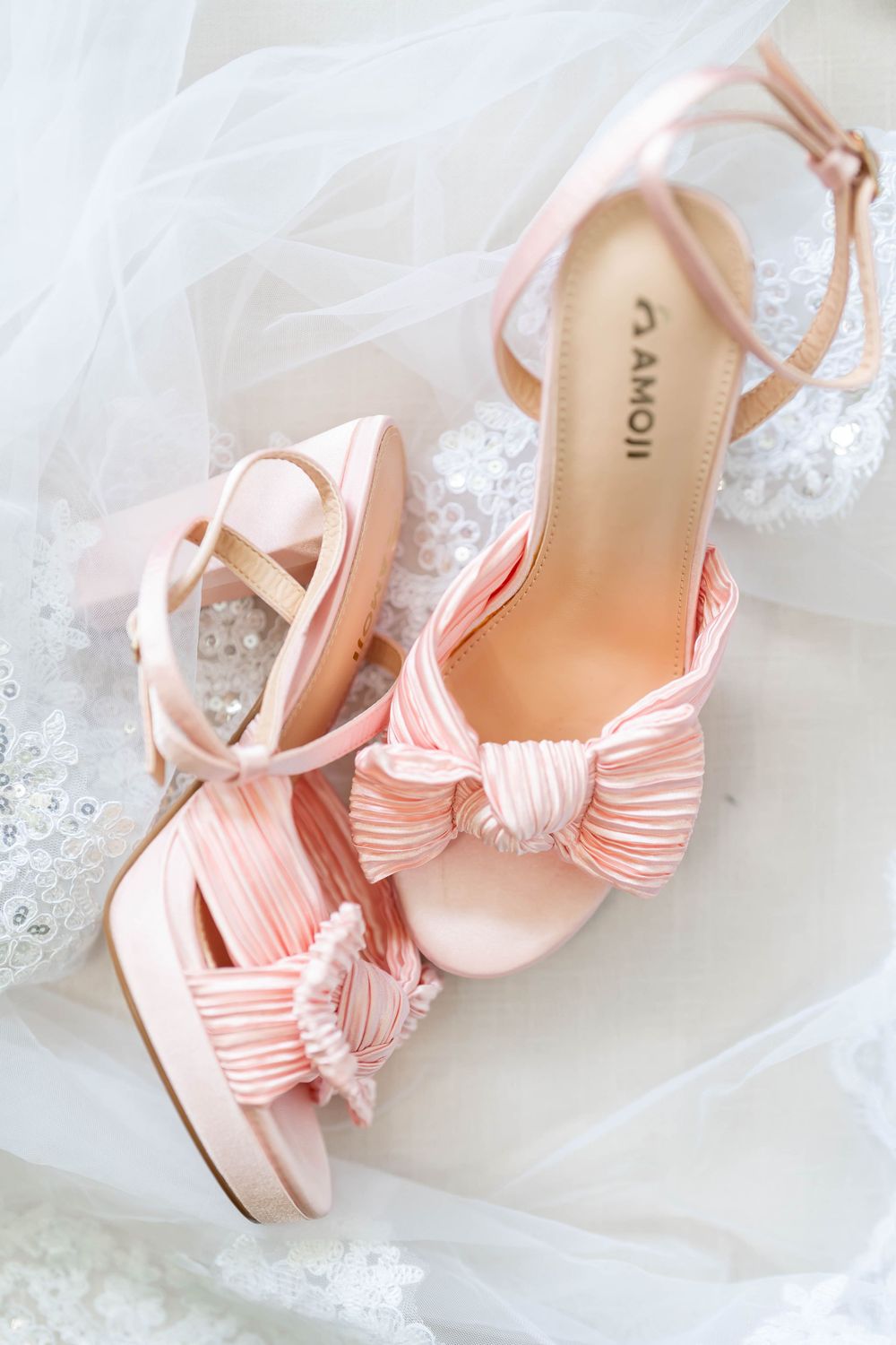 Pink satin wedding heels with bow detail by Amoi, displayed on white bridal veil fabric.