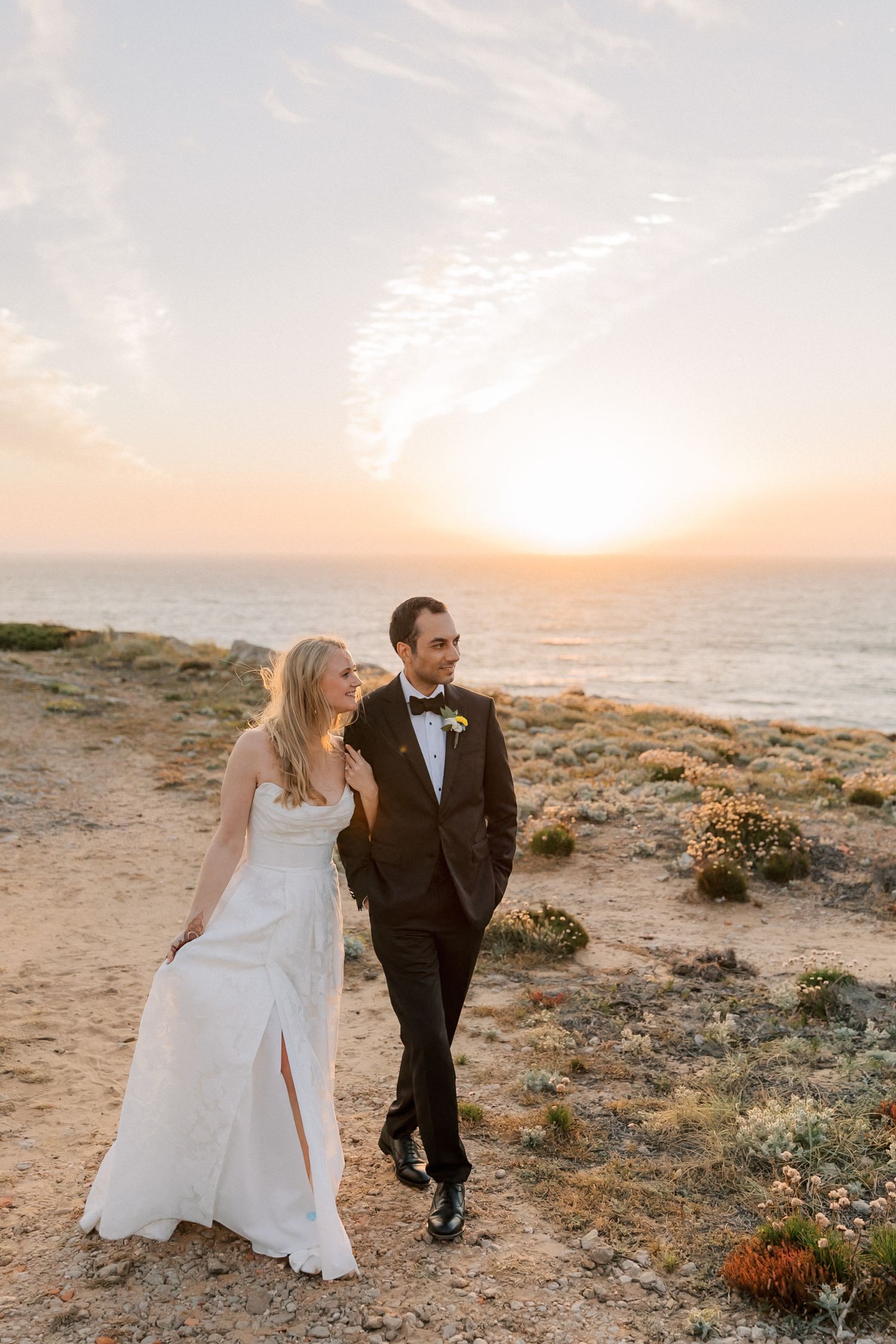 Bride and groom walking along the Atlantic coastline during golden hour after their destination wedding ceremony in Portugal.