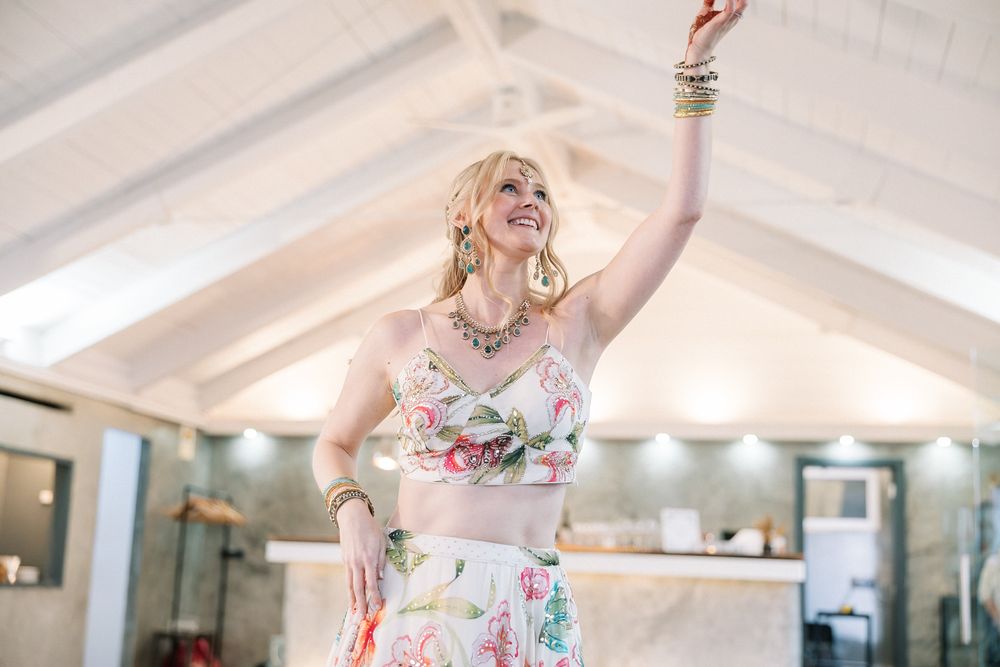 Joyful bride performing a traditional Sangeet dance during an Indian wedding celebration overlooking the Atlantic Ocean in Portugal.