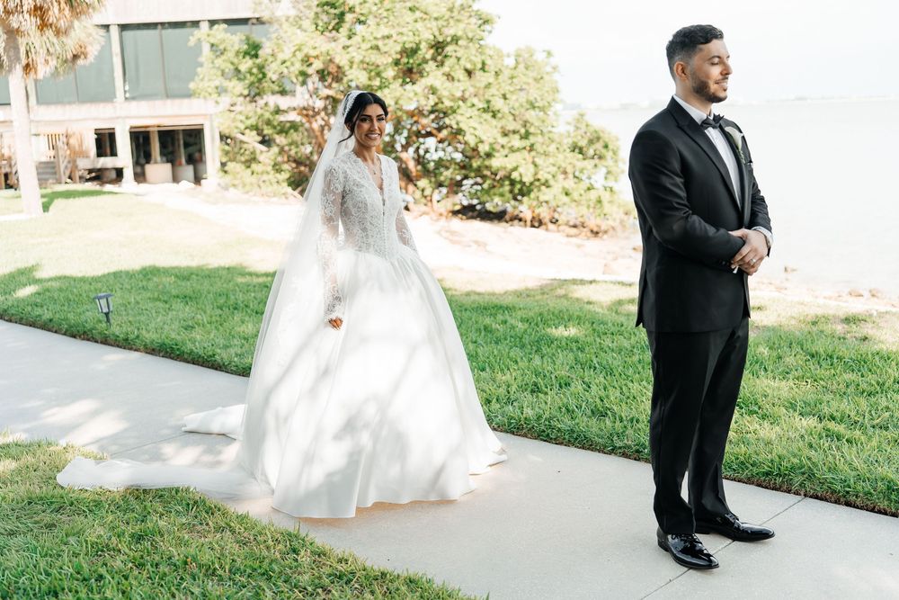 Bride in white ball gown celebrates emotional first look moment with groom in black tuxedo at waterfront venue.