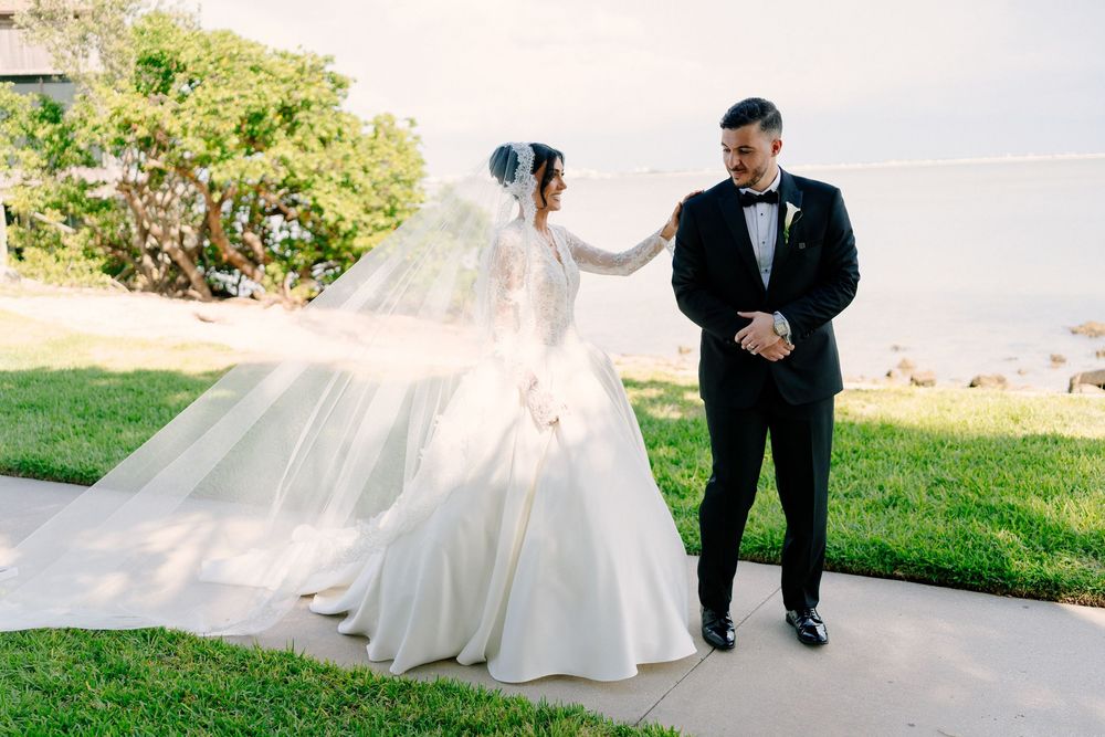 Groom admiring bride as her veil flows in the wind during outdoor first look.
