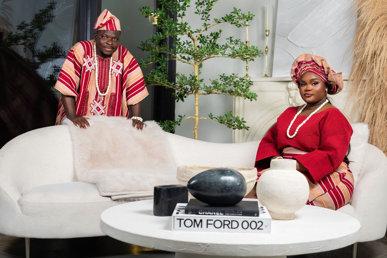 Couple in traditional Nigerian attire seated on white sofa with Tom Ford book on coffee table.