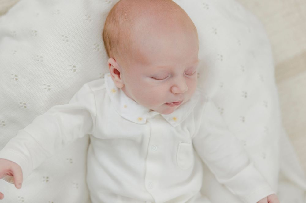 Peaceful newborn baby sleeping in white outfit on soft ivory blanket, serene infant portrait photography.