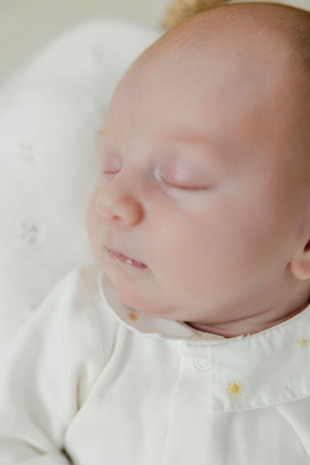 Close-up portrait of a sleeping newborn baby with delicate features, wearing a white outfit with tiny star details.