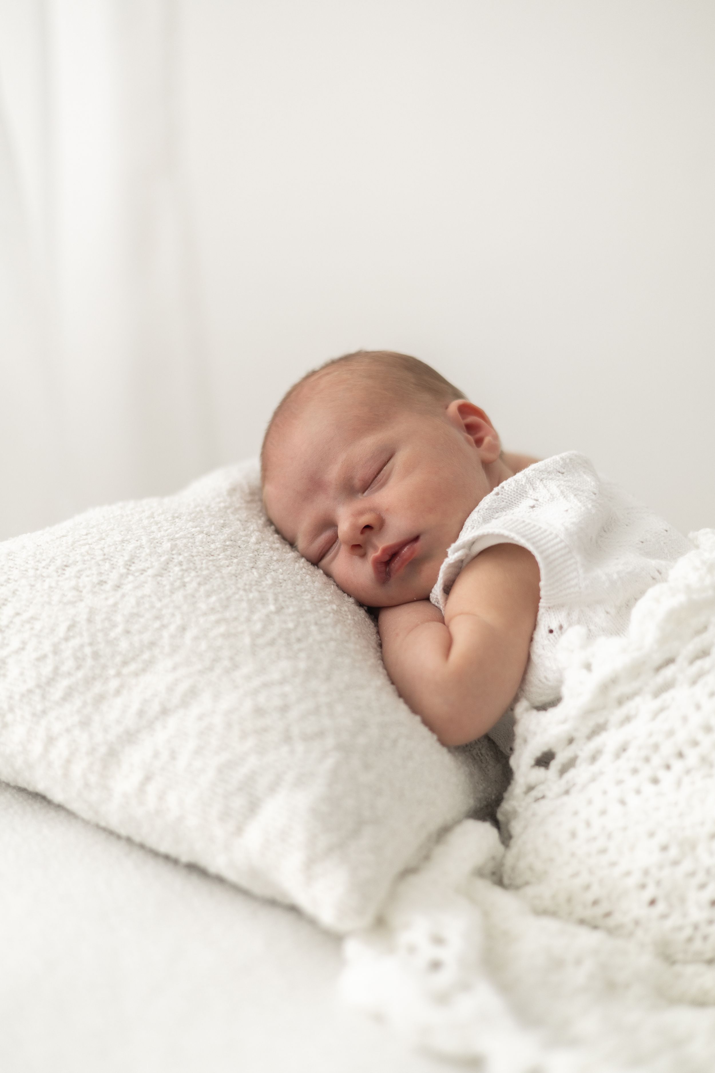 Peaceful newborn baby sleeping on a white knit pillow wrapped in a soft white blanket relaxed newborn photoshoot Nottingham
